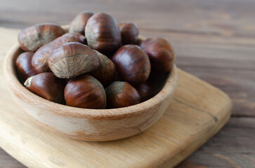 Edible raw chestnuts in a wooden bowl on the table. The concept of autumn food. Street food. Selective focus. Horizontal orientation.