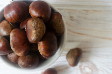 Edible raw chestnuts in a ceramic bowl on the wodden table. The concept of autumn food. Street food. Selective focus. Horizontal orientation. Top view. Copy space