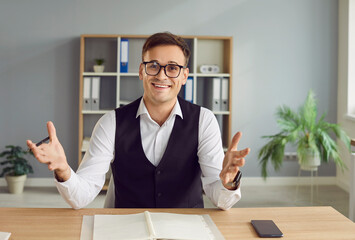 A young attractive businessman working in office looking at camera having video call sitting at the desk on workplace. Satisfied confident man chatting online or having video conference call.