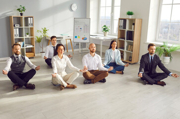 Smiling young business people meditating and having a rest in office sitting on floor in Lotus pose...