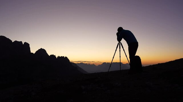 one man, photographer taking pictures alone in the mountains in the evening with colorful sky waiting for the night to come

