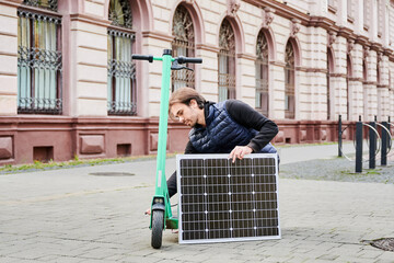 Man connects solar panel to electric scooter for charge. Integration of solar power as sustainable energy source for charging electric scooters, promoting eco-friendly urban transportation.