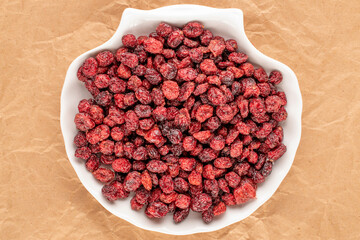 Dried cranberries with ceramic dishes on kraft paper and top view, macro.