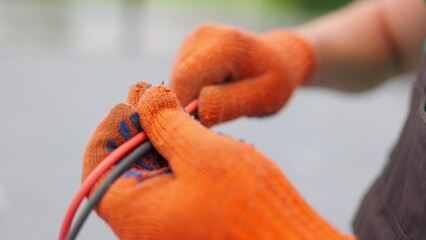 An electrician worker holds a red and black high-voltage electric cable, checks the quality of the cables. Connecting electrical cables. Close up of male hands in protective gloves holding cable.