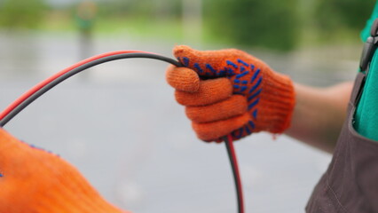 An electrician worker holds a red and black high-voltage electric cable, checks the quality of the cables. Connecting electrical cables. Close up of male hands in protective gloves holding cable.