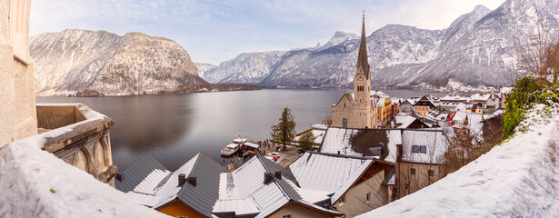 A panoramic winter view of Hallstatt village with snow-covered rooftops overlooking Hallstatt Lake and the surrounding mountains in the Austrian Alps