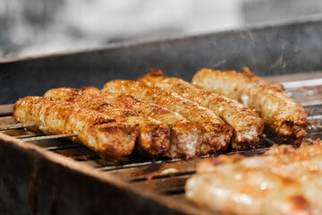 Close-up of grilled sausages sizzling on barbecue showcasing the charred and golden texture of the meat as it cooks over the fire