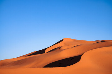 Desert landscape of sand dunes with traces of wheeled vehicles at sunset.  Erg Chebbi. Merzouga. Sahara desert. Morocco. Africa.