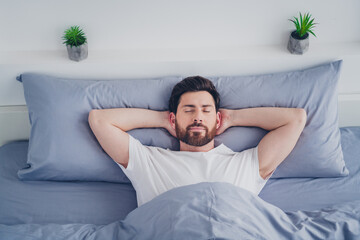 Photo of attractive funny young man nightwear pajama lying bed arms behind head indoors house apartment room