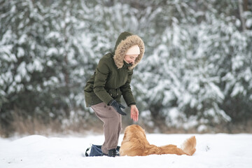 Beautiful young girl walking with a purebred retriever near a snowy forest in winter.