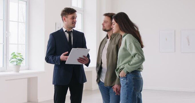 Young family couple choosing new house or apartment, meeting with real estate agent, discussing mortgage contract agreement, trying to take decision and make right choice of accommodation
