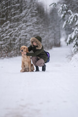 Obraz premium Beautiful young girl walking with a purebred retriever near a snowy forest in winter.