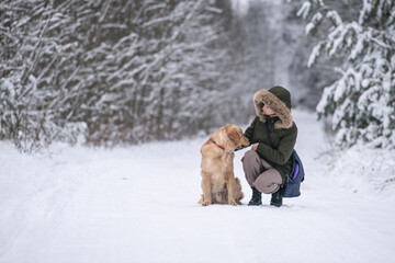 Beautiful young girl walking with a purebred retriever near a snowy forest in winter.