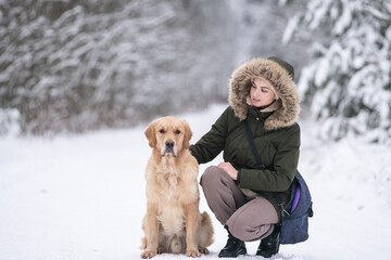 Beautiful young girl walking with a purebred retriever near a snowy forest in winter.