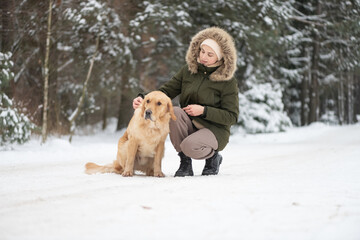 Beautiful young girl walking with a purebred retriever near a snowy forest in winter.