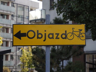 Obraz premium Yellow detour road sign for cyclists against urban architecture background