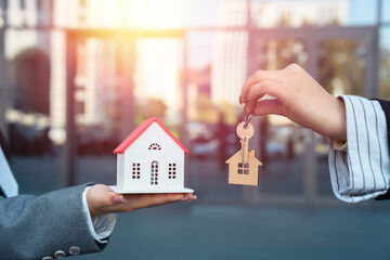 Two business women, one holding a small wooden house, the other a key, house sale, business concept