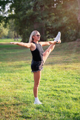 Sporty woman doing Utthita Hasta Padangusthasana number one, exercising in park standing on one leg with left leg up in casual clothes, full length view