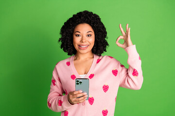 Photo of pretty young girl hold gadget show okey wear strawberry print pink outfit isolated on green color background