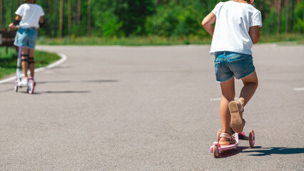 Seasonal children's sports. Healthy childhood lifestyle. Summer holidays. Little girl, child riding a scooter on the road in the park outdoors.