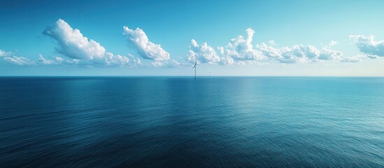 A single wind turbine stands tall in the vast expanse of the ocean, with a clear blue sky above and fluffy white clouds.