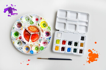 Paint stained plastic artist palette for painting. Used artist palette with paint splashes on white background. Set of watercolor paints on white background. Open plastic box with 12 watercolor half-c