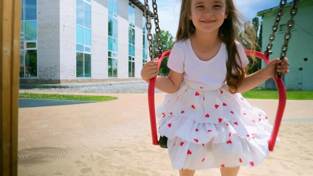 Child girl swinging on swing in park, kid having fun , playing on outdoor public playground, kids play on school or kindergarten yard, active kid on colorful swing, healthy summer activity for childre