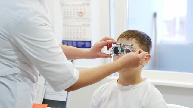 Boy doing eye test checking examination with optometrist in optics store, kid boy choosing eyeglasses in optics store