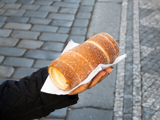 Trdelník or spit cake from Czechia. Holding the fresh and warm food rolled in sugar an cinnamon. Traditional food in Prague, Czech Republic.