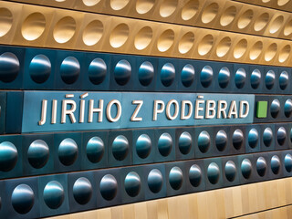 Jiřího z Poděbrad metro station in Prague, Czechia. Sign of the location name in the subway tunnel. Yellow and blue aluminum shapes are mounted to the wall. Public transportation in the big city.