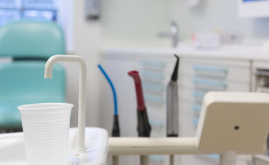 Close-up of disposable white plastic mouth rinse cups, aspirators probes and air blower attachments during dental procedures in dental clinic. Selective focus. Dentist's water rinse cup top lip filler