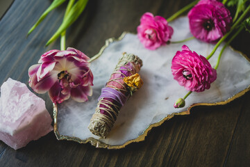 overhead photo of pink flowers and sage smudge stick with crystals