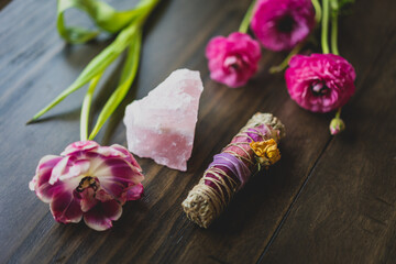 sage smudge stick, rose quartz, and flowers on a wood table