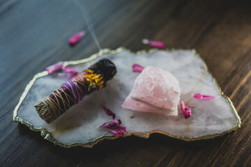 burning sage smudge stick on table with crystals and flower petals