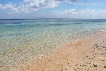 Tranquil beach scene with crystal clear water and a partially cloudy sky.