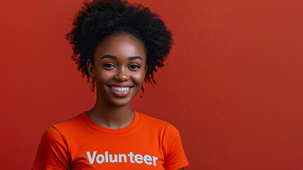 Smiling young black woman with curly hair wearing an orange volunteer t-shirt, isolated on a red background