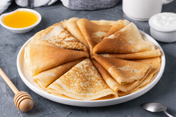 Stack of traditional russian pancakes blini with honey and sour creamon gray background.
