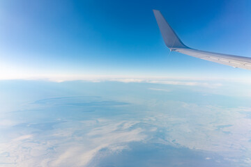Fototapeta premium View from the airplane window at a beautiful blue clear sky, earth, sea and the airplane wing