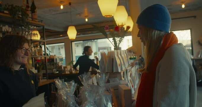 A female customer and woman barista or cafe owner have a friendly chat and interaction over the counter. Staff employee and customer ordering drinks, get served tea in scandinavian cafe