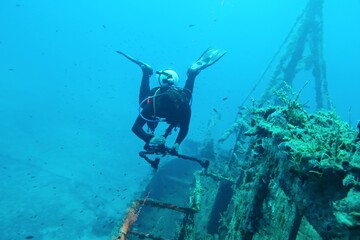 Deep blue ocean with underwater photographer and old shipwreck. Sunken boat, remains in the ocean....