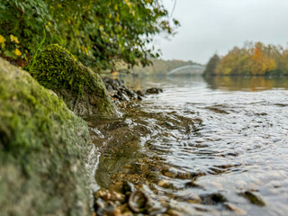 Smooth riverbank rocks create a tranquil setting along a winding river with lush greenery and gentle water ripples on a misty autumn day
