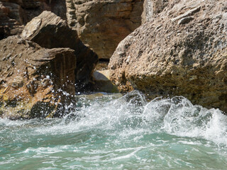 Dynamic shot of ocean waves splashing against rocky cliffs. The detailed textures of the rocks highlight natural erosion, contrasting with the movement of foamy water below.