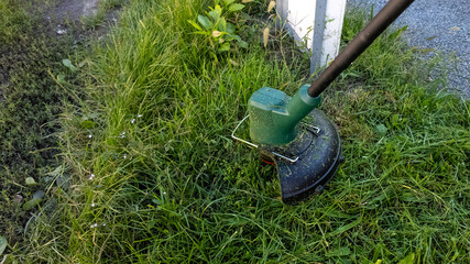 Green electric grass trimmer cutting overgrown lawn, representing lawn care and gardening solutions