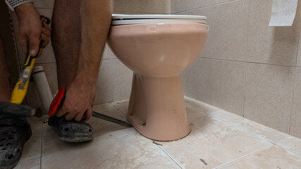 A person performs DIY toilet repair with tools, addressing plumbing issues in a bathroom setting