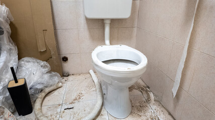 A dirty, unmaintained toilet in a cluttered bathroom illustrates plumbing issues and sanitation...