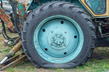 one big heavy black rubber patterned tire old iron green disk flat industrial round rear tractor wheel stands on the ground during the day outdoors
