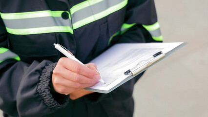 Worker Writing on Clipboard for Inspection. Close-up of a worker in reflective safety gear writing...