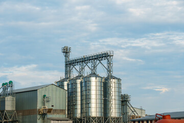 silver silos on agro manufacturing plant for processing drying cleaning and storage of agricultural products, flour, cereals and grain. Large iron barrels of grain. Granary elevator