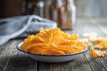 Crispy potato chips on plate on wooden table.