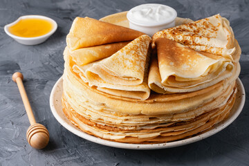 Stack of traditional russian pancakes blini with honey and sour creamon gray background